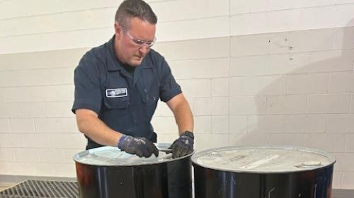 Gloved Enviro-Safe technician working on the lid of a black drum beside a second drum.