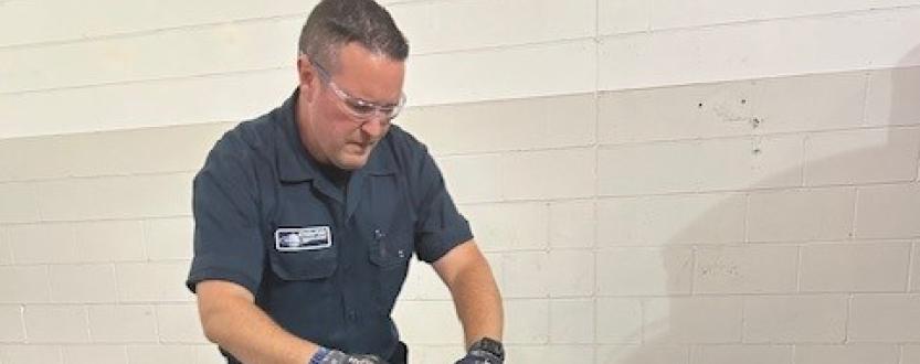 Enviro-Safe technician wearing safety glasses and gloves at a waste handling workstation.